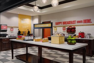 Un área de desayuno con mostrador, estación de gofres y un cartel que dice 'HAPPY BREAKFAST STARTS HERE'.