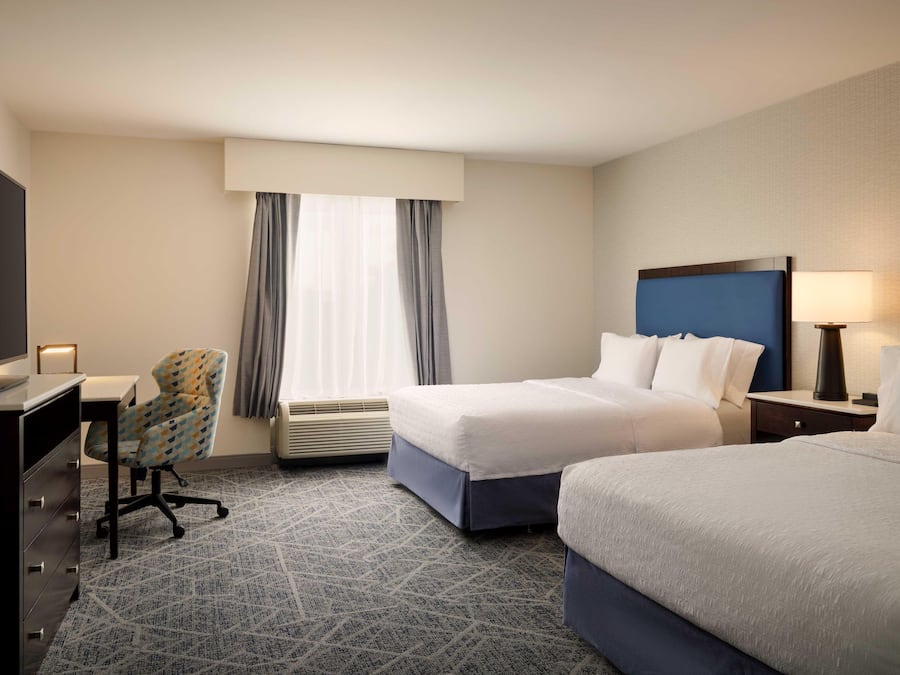 A hotel room with two beds, a desk with a chair, a TV, and a window with curtains.