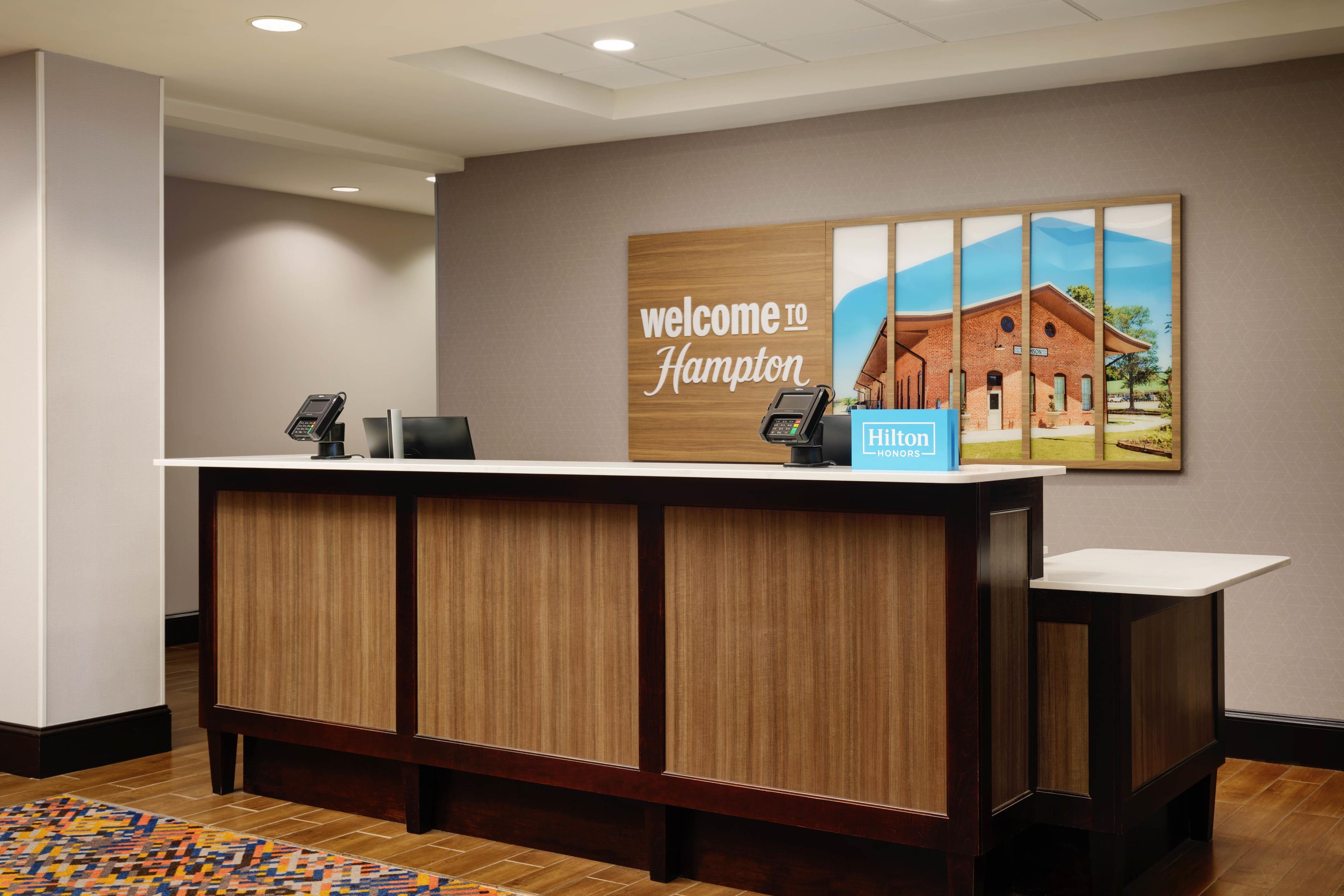 A reception desk with a 'Welcome to Hampton' sign, a phone, and a 'Hilton' sign.