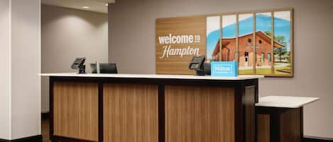 A reception desk with a 'Welcome to Hampton' sign, a phone, and a 'Hilton' sign.