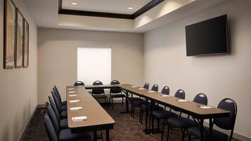 A conference room with a long table, chairs, a flat-screen TV, and framed pictures on the wall.