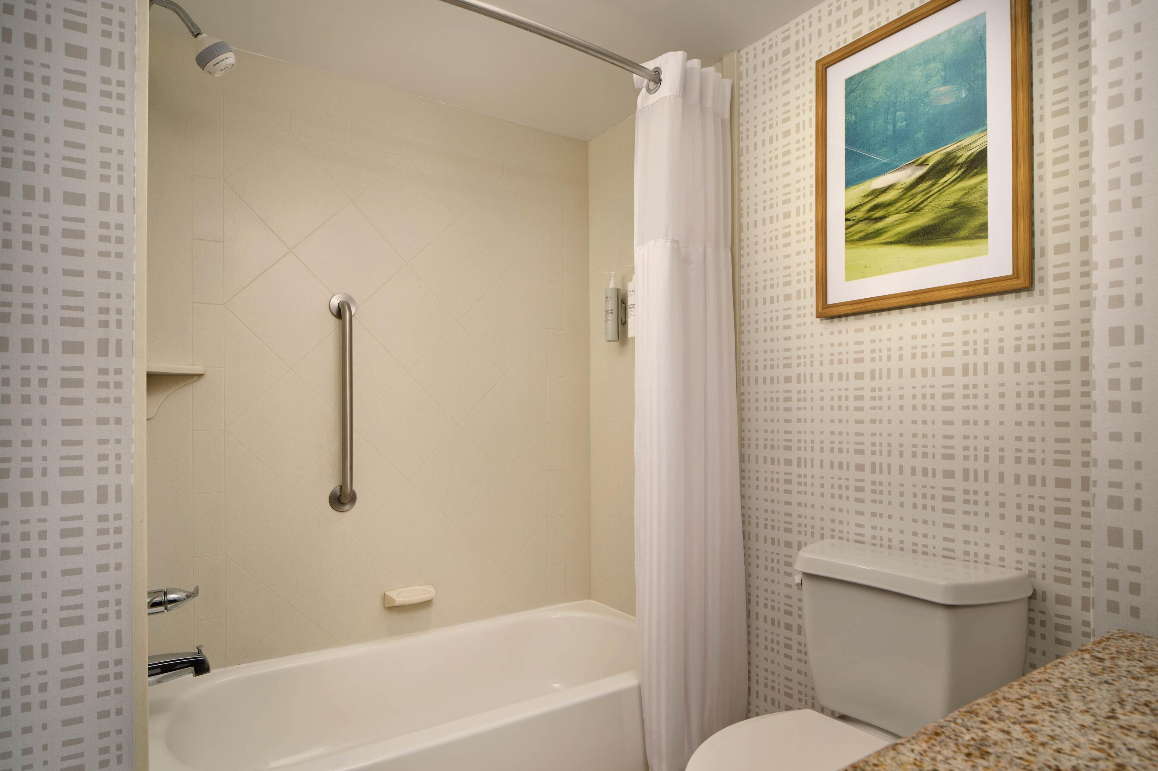 Un baño con bañera, inodoro, cortina de ducha y un cuadro en la pared.