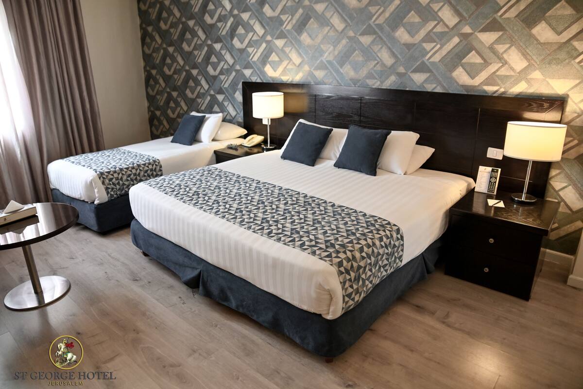 A hotel room with two beds, a desk, and a patterned wall.