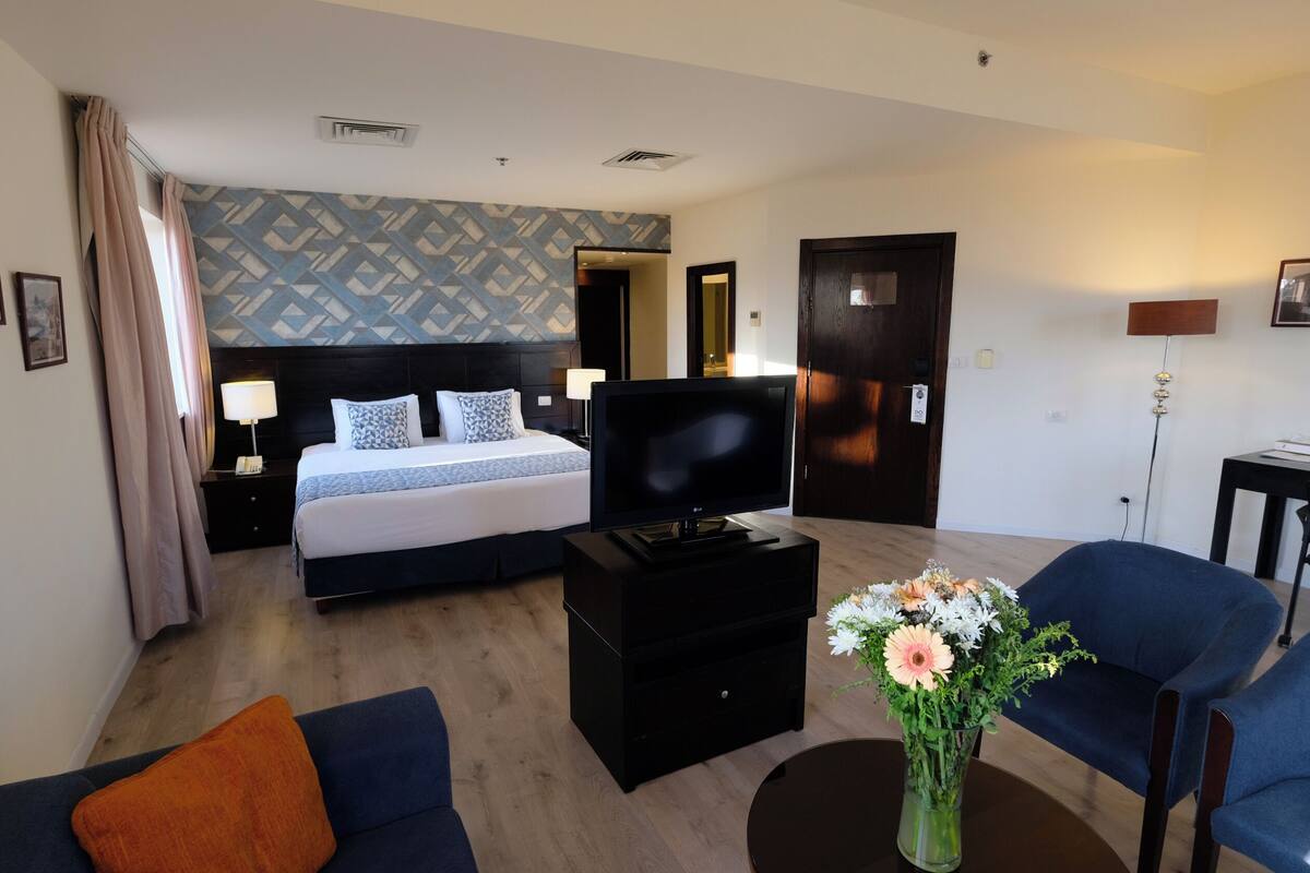 A hotel room with a bed, a TV, a desk, a chair, and a vase of flowers.