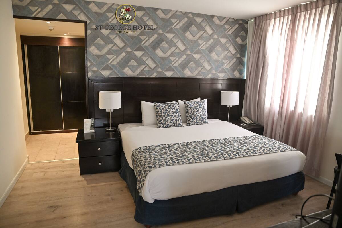 A hotel room with a large bed, two bedside tables, a wardrobe, and a patterned wall.