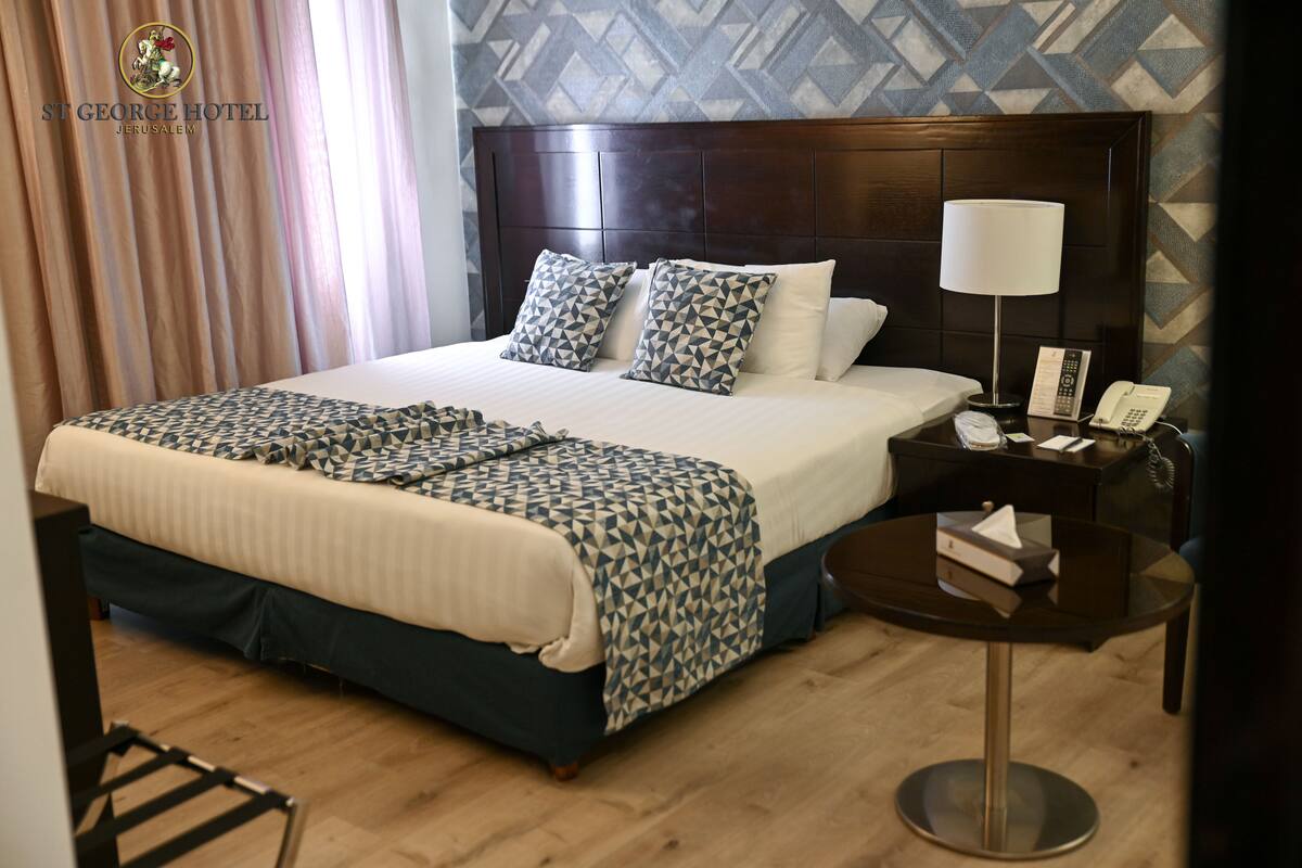 A hotel room with a large bed, a bedside table with a lamp, a phone, and a small table with a tissue box.
