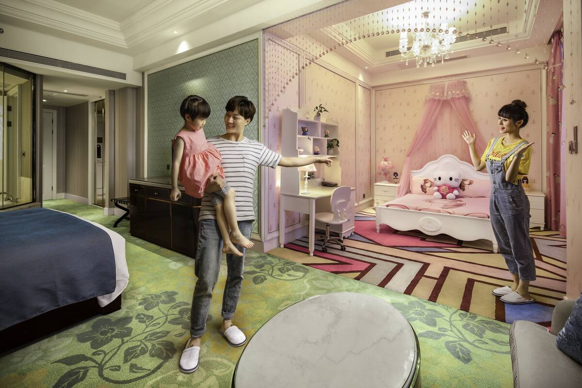 A hotel room with a bed, a desk, a chair, a vanity, and a pink canopy bed.