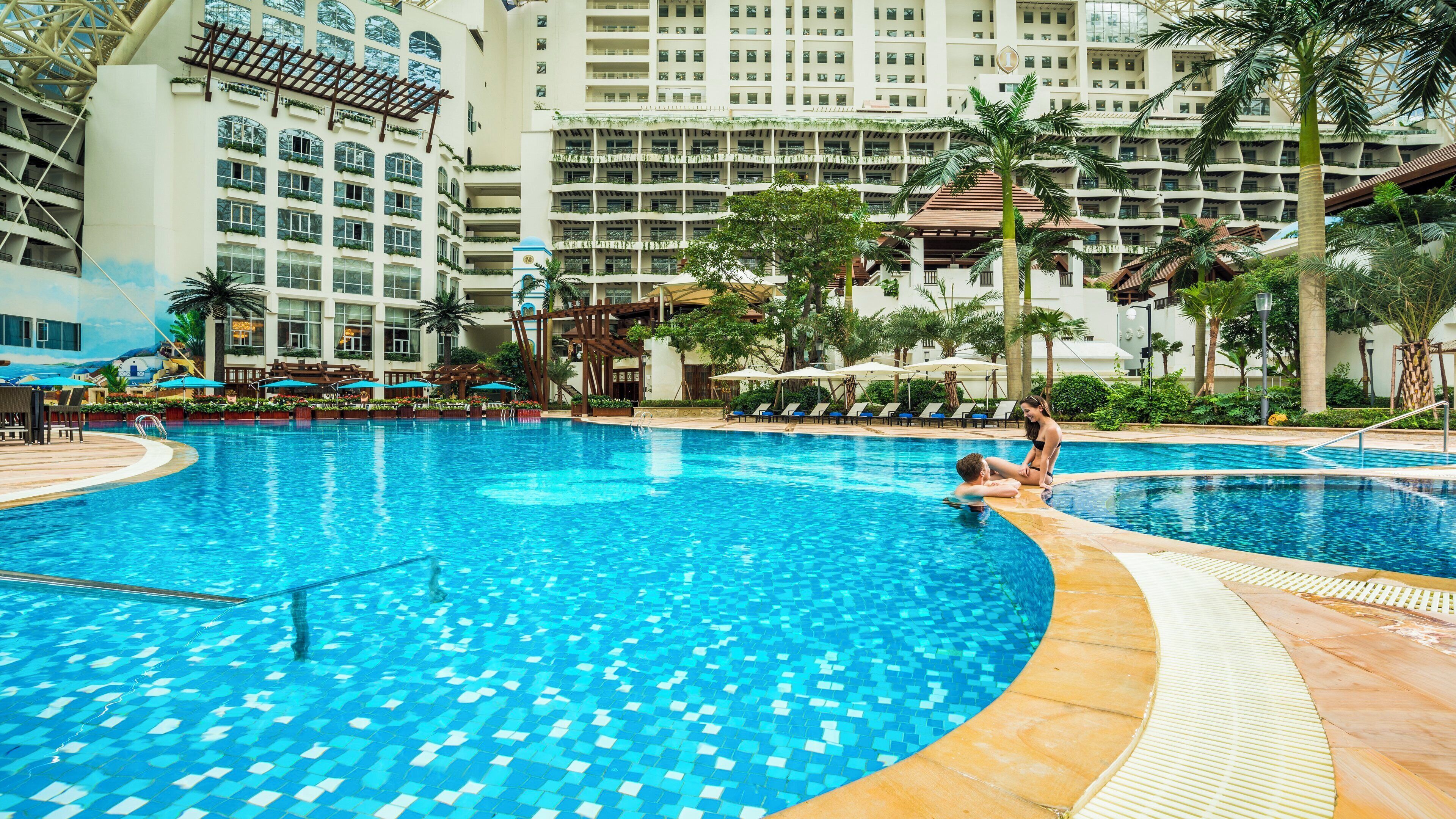 Una amplia piscina cubierta con suelo de baldosas, rodeada de sillas de descanso y sombrillas.