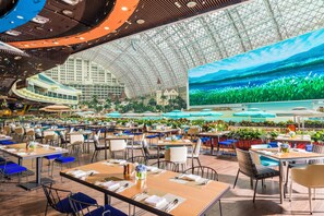 A spacious indoor dining area with multiple tables and chairs, a large digital screen displaying a nature scene, and a view of a pool and buildings in the background. - InterContinental Chengdu Global Center by IHG (Chengdu)