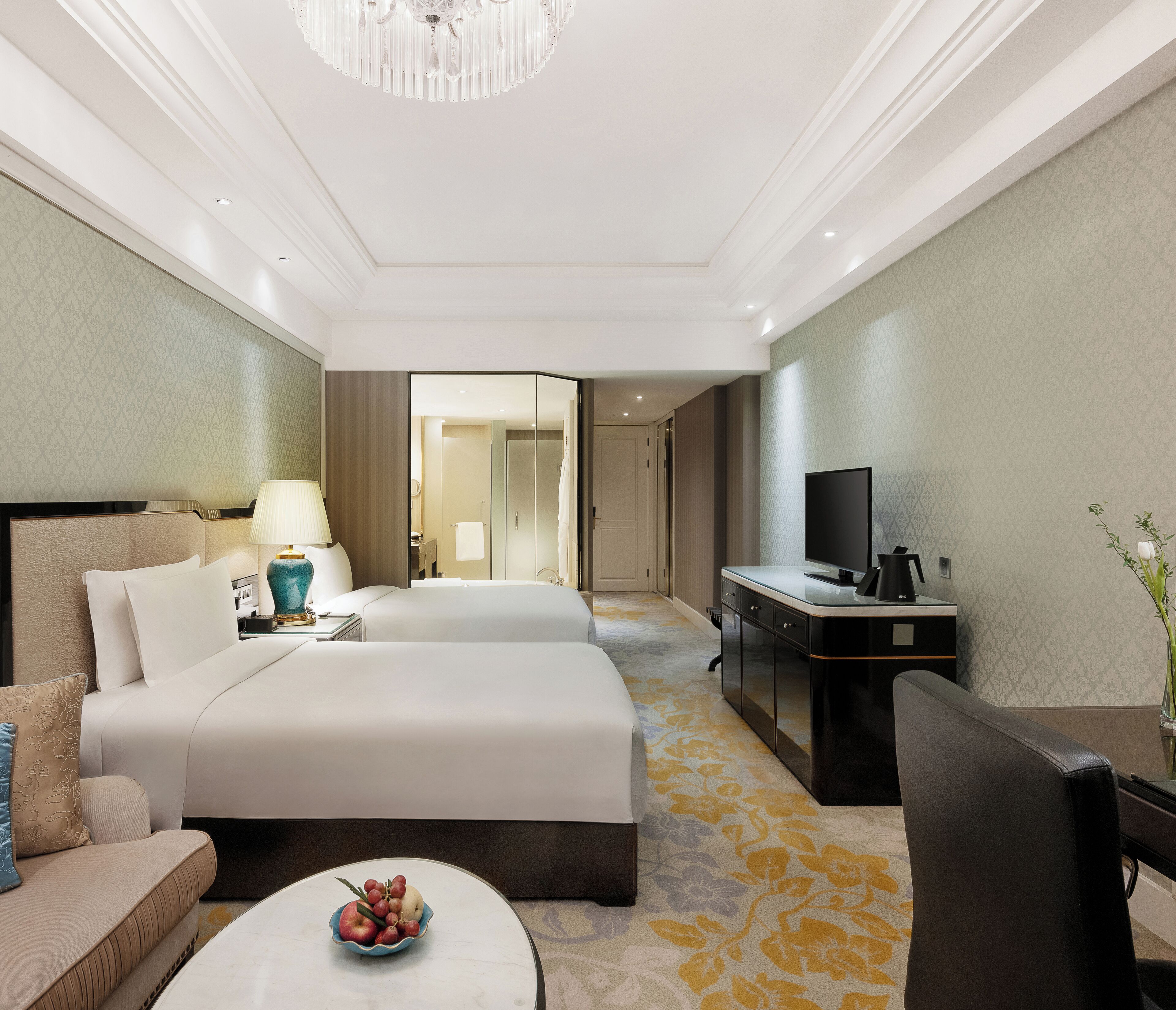 A hotel room with a bed, a desk, a TV, a lamp, and a small table with fruit.