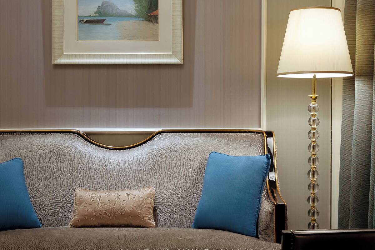 A hotel room with a textured sofa bed, a framed painting on the wall, a standing lamp, and a dark leather armchair.