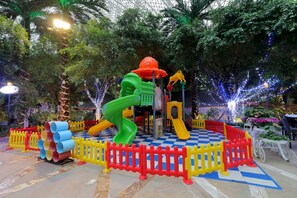 Un parque infantil con toboganes y estructuras para escalar, rodeado de un suelo a cuadros y una cerca roja y amarilla.