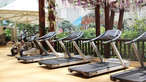 A row of treadmills in a gym area with a view of greenery and a building in the background.