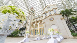 A grand building with a glass roof and a tower, surrounded by white flowers and palm trees.