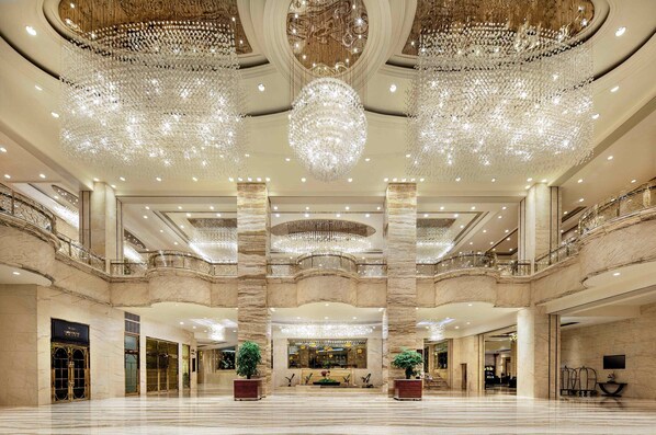 Un amplio vestíbulo con suelos de mármol, grandes candelabros y una imponente escalera.