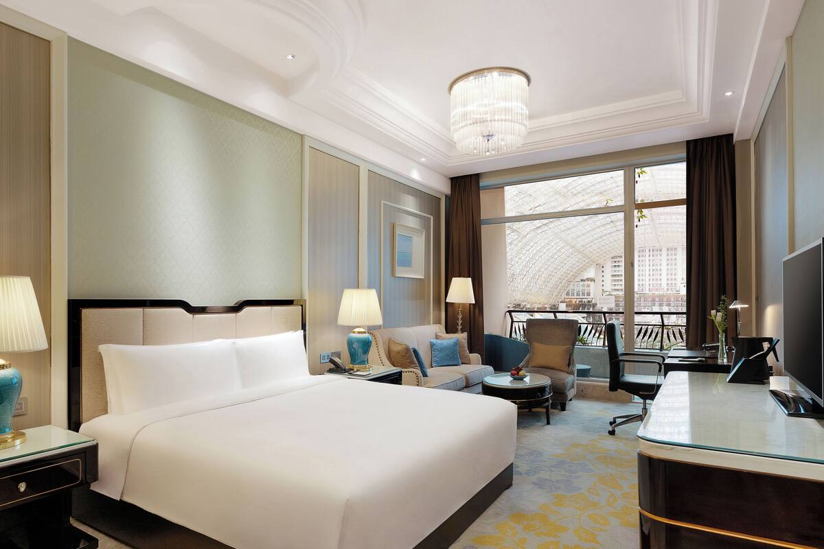 A hotel room with a large bed, a desk, a sofa, and a balcony with a view of the city.