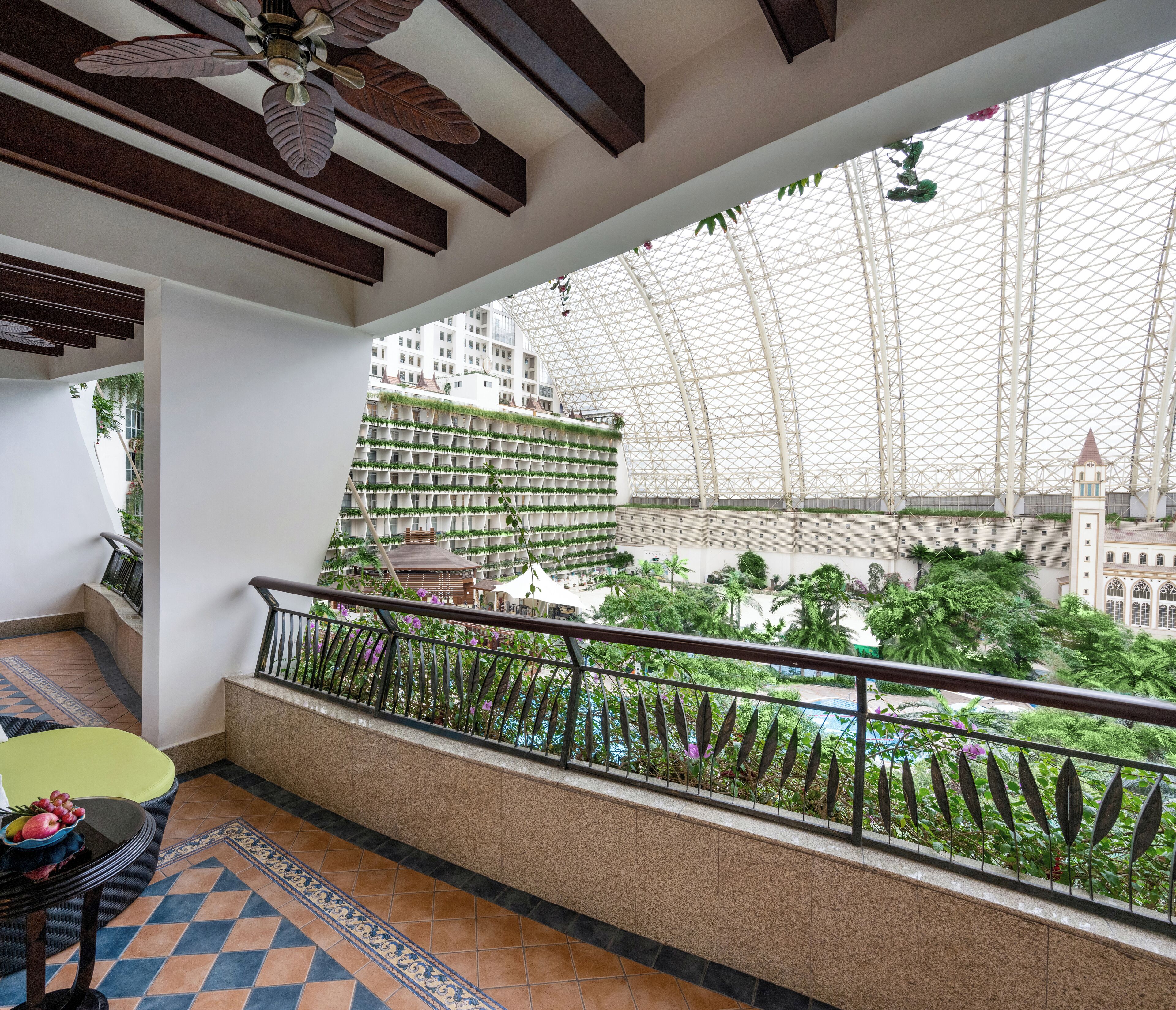 A balcony with a view of a building with vertical gardens, a tiled floor, and a railing.