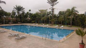 Relax by the pool surrounded by lush tropical plants and palm trees, with lounge chairs and a tiled deck.