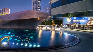 Una piscina moderna al aire libre con esculturas geométricas, sillones de descanso y una zona de bar.