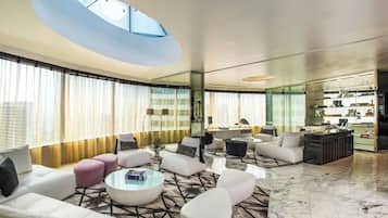 A modern living room with a high ceiling, large windows, and a central seating area.