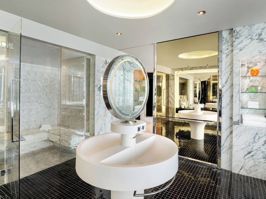 A modern bathroom with a large mirror, glass shower enclosure, and marble flooring.