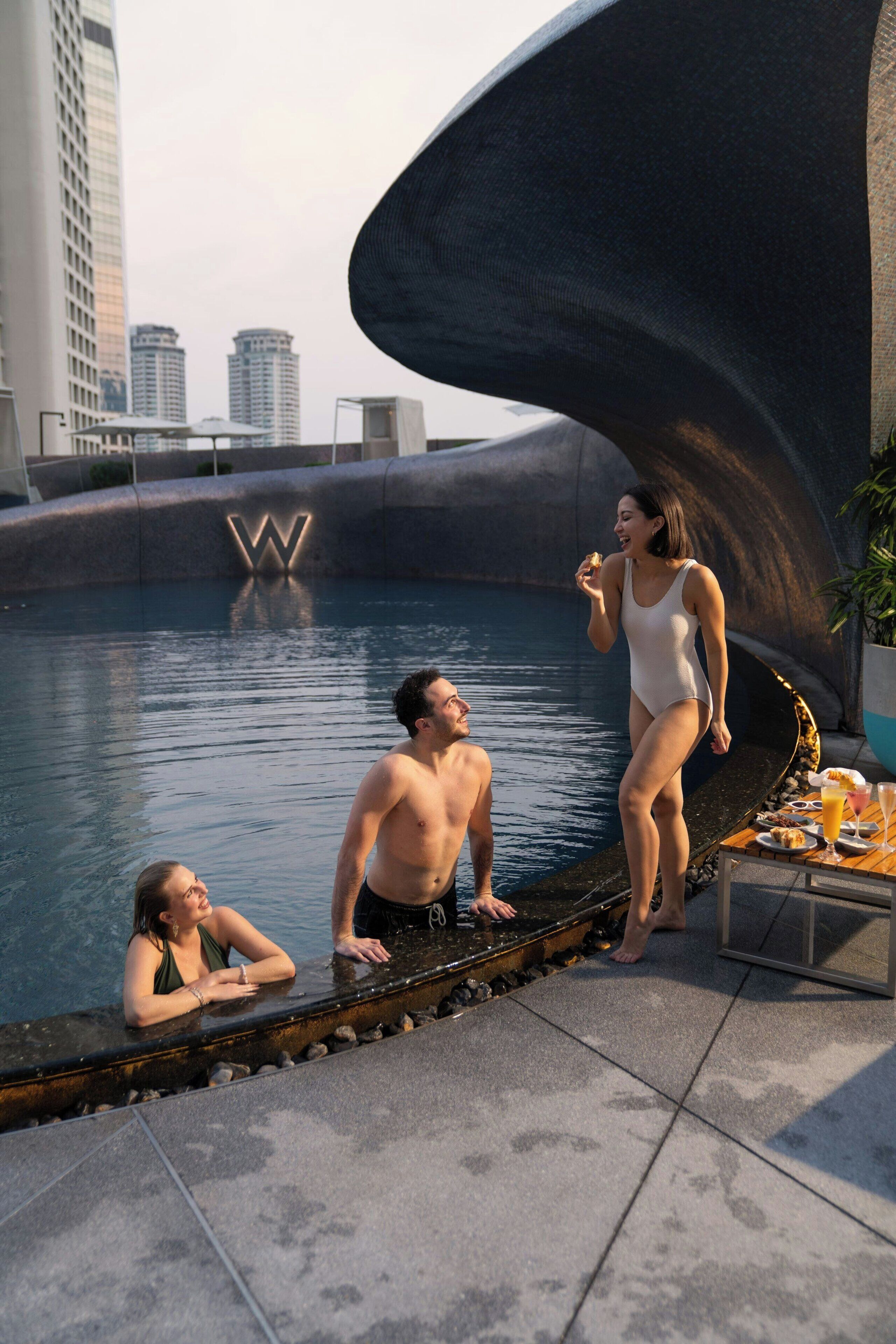 A poolside area with a modern architectural design, including a large curved structure and a visible 'W' logo.