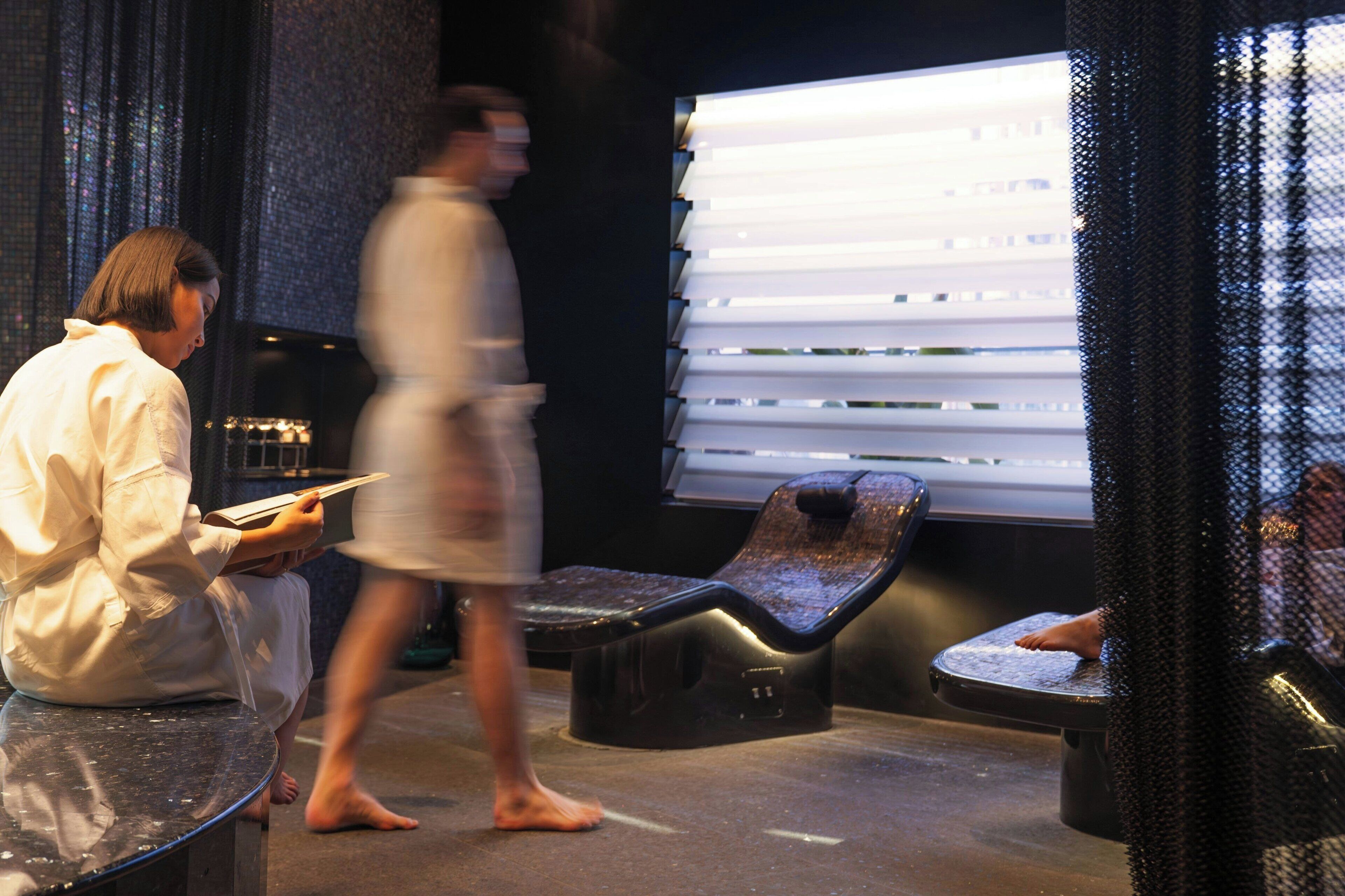 A spa area with a massage chair, a person reading, and a walking individual.
