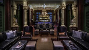 Un lobby lujoso con columnas ornamentales, una zona de bar, sofás de cuero y una araña.