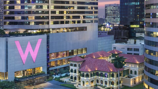 Un hotel moderno con un llamativo logo 'W', rodeado de edificios de gran altura y un edificio clásico con techo rojo.