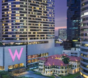 A modern hotel with a prominent 'W' logo, surrounded by high-rise buildings and a classical building with a red roof. - W Bangkok (Bangkok)