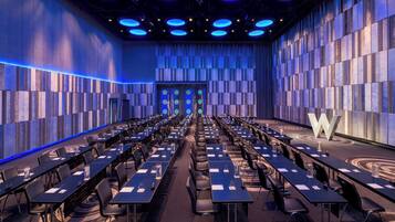 A conference room with rows of tables and chairs, a large 'W' logo on the wall, and a blue ambient light.