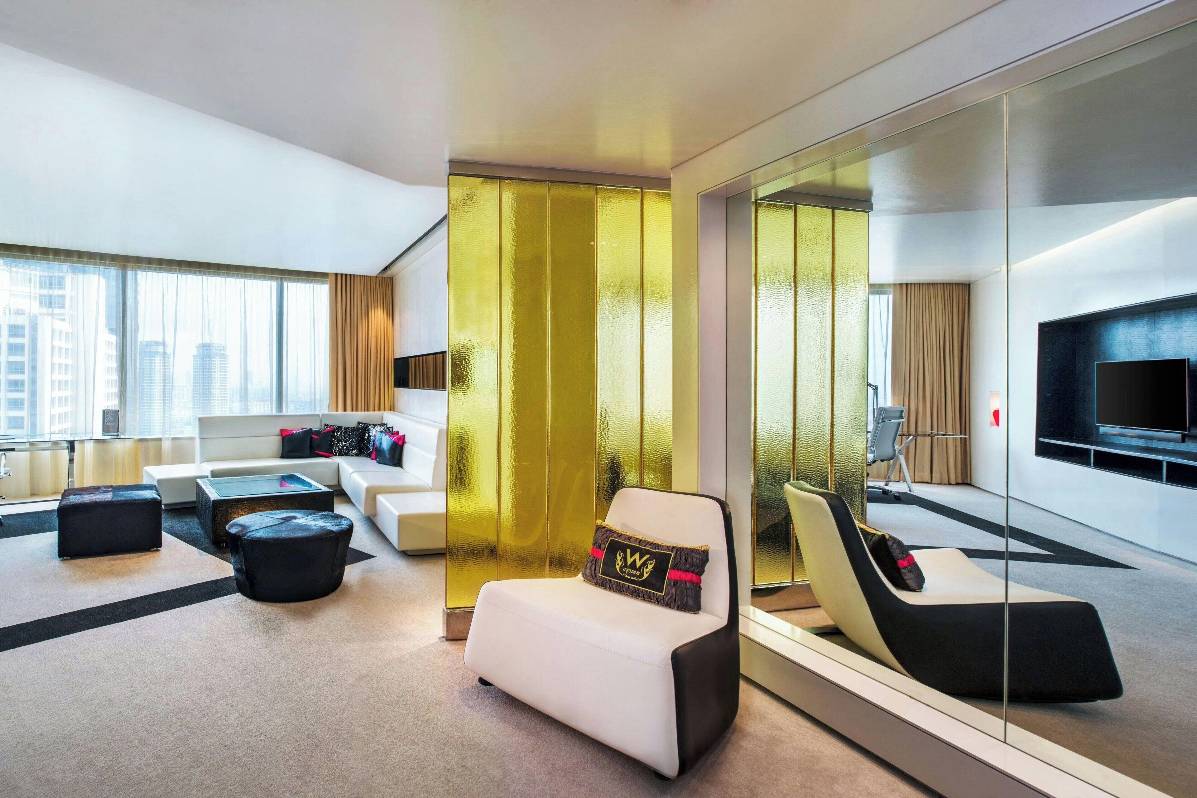 Een moderne hotelkamer met een bank, een poef en een stoel met een kussen.