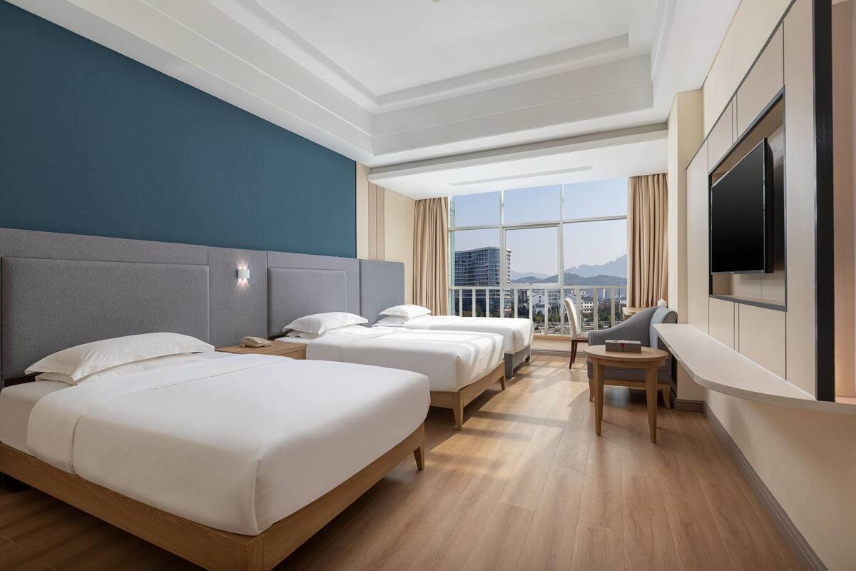 Habitación de hotel con dos camas, televisión, balcón con vistas a la ciudad y escritorio.