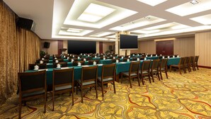 Un salón de conferencias con filas de mesas y sillas, una pantalla grande y una alfombra estampada.