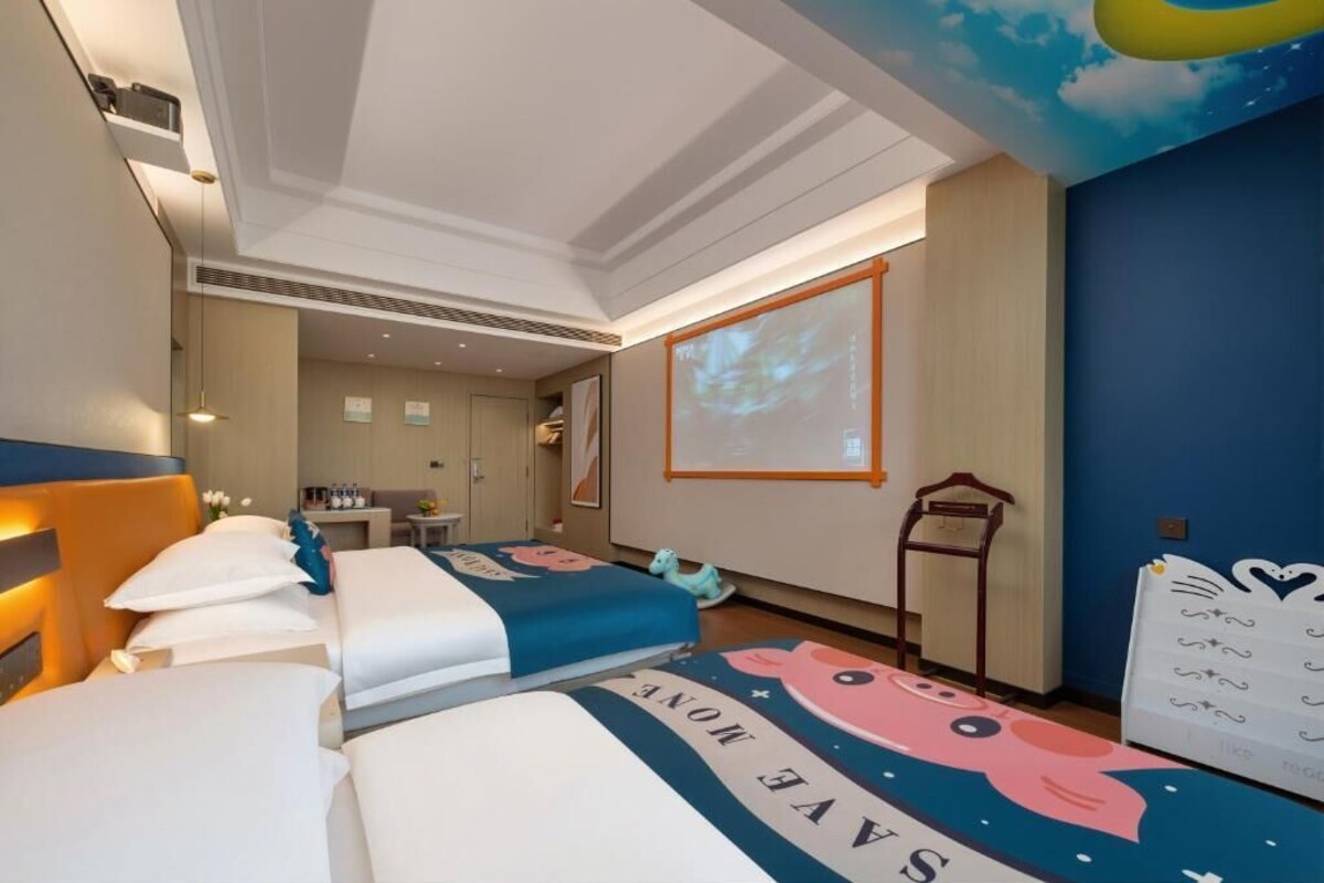 A hotel room with two beds, a projector screen, a desk, and a wall with a cartoon character design.