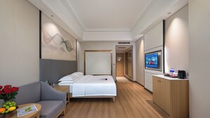 Habitación de hotel con cama, sofá, televisión, una mesita con un jarrón de flores y un armario.