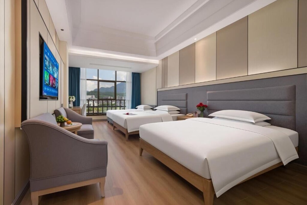 A hotel room with two beds, a sofa, a TV, and a view of the outdoors.