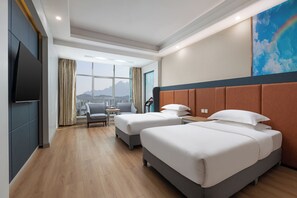 Habitación de hotel con dos camas, un televisor, vistas a montañas y un paisaje urbano.