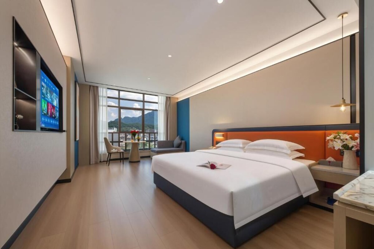 A hotel room with a bed, bedside table, TV, and a view of the outdoors.