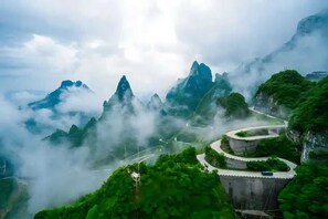A winding mountain road surrounded by lush greenery and towering peaks, with a road sign indicating a scenic route. - Ramada by Wyndham Zhangjiajie Tianmen Mountain (Zhangjiajie)