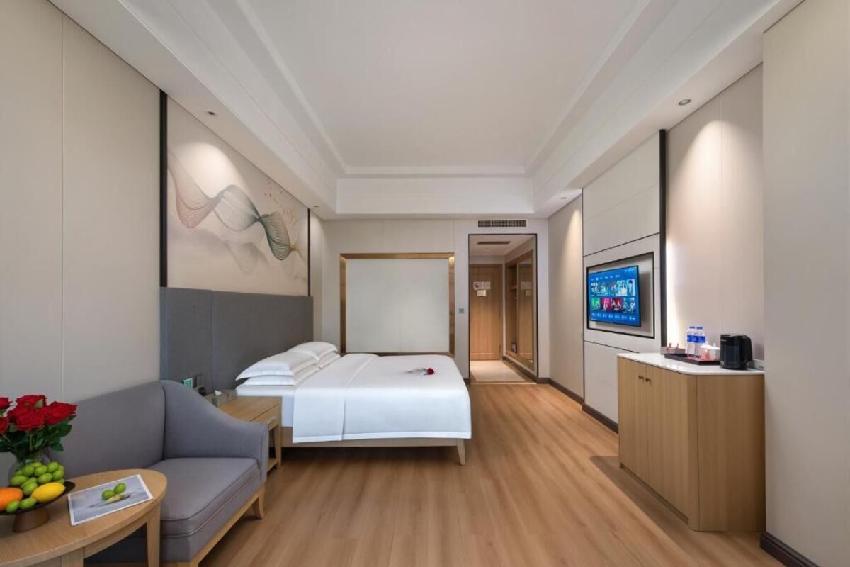 A hotel room with a bed, a sofa, a TV, a desk, and a cabinet.