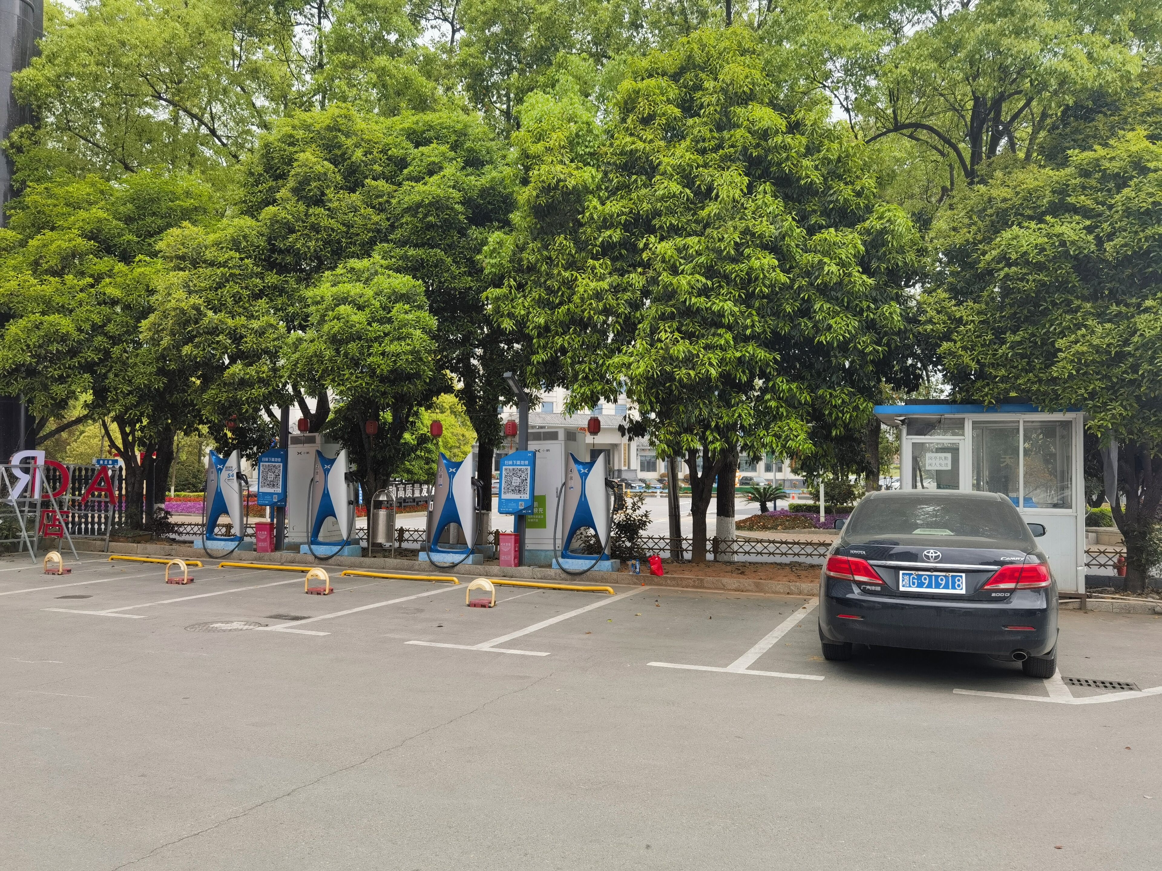 A parking area with a car, trees, and a small kiosk.