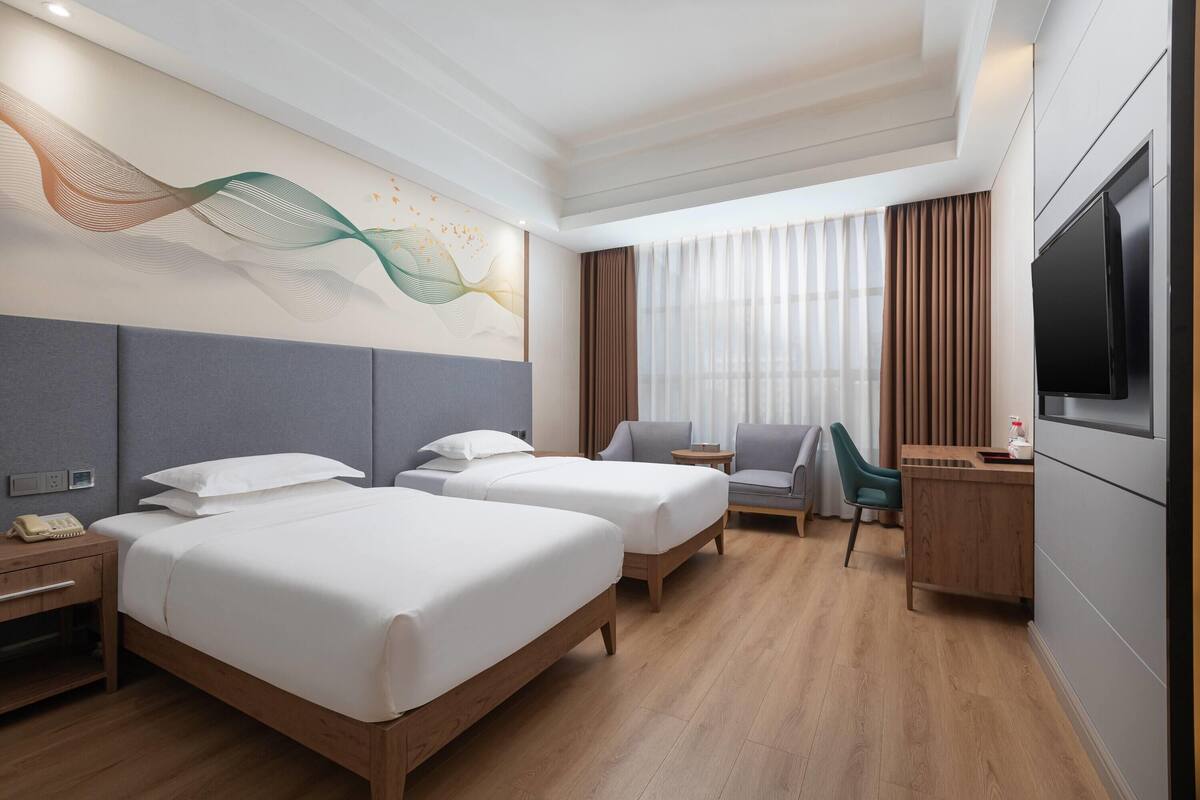 Habitación de hotel con dos camas, un escritorio, una silla, un televisor y un mural decorativo en la pared.