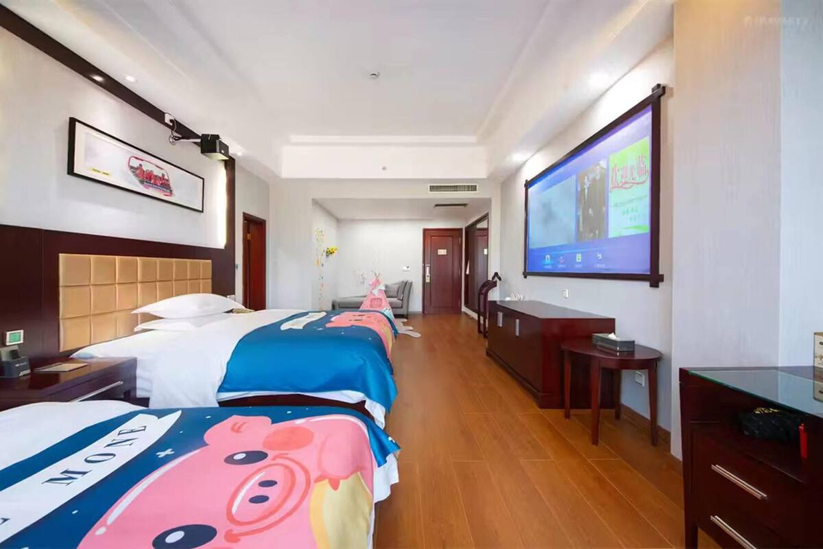 Habitación de hotel con tres camas, televisión, escritorio y armario.