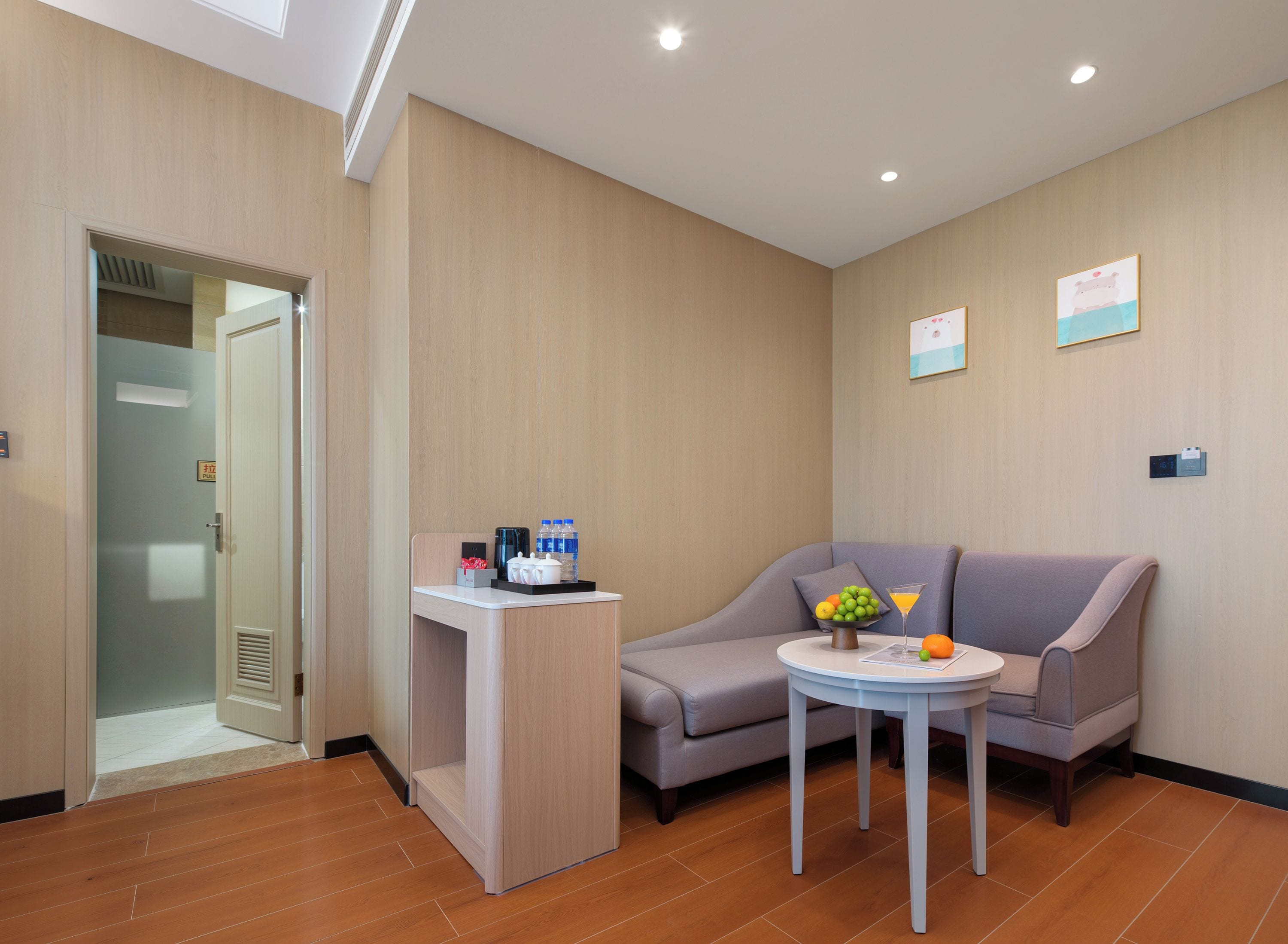 Une chambre d’hôtel avec un canapé, une petite table avec une boisson, et un bureau avec une machine à café et des bouteilles d’eau.