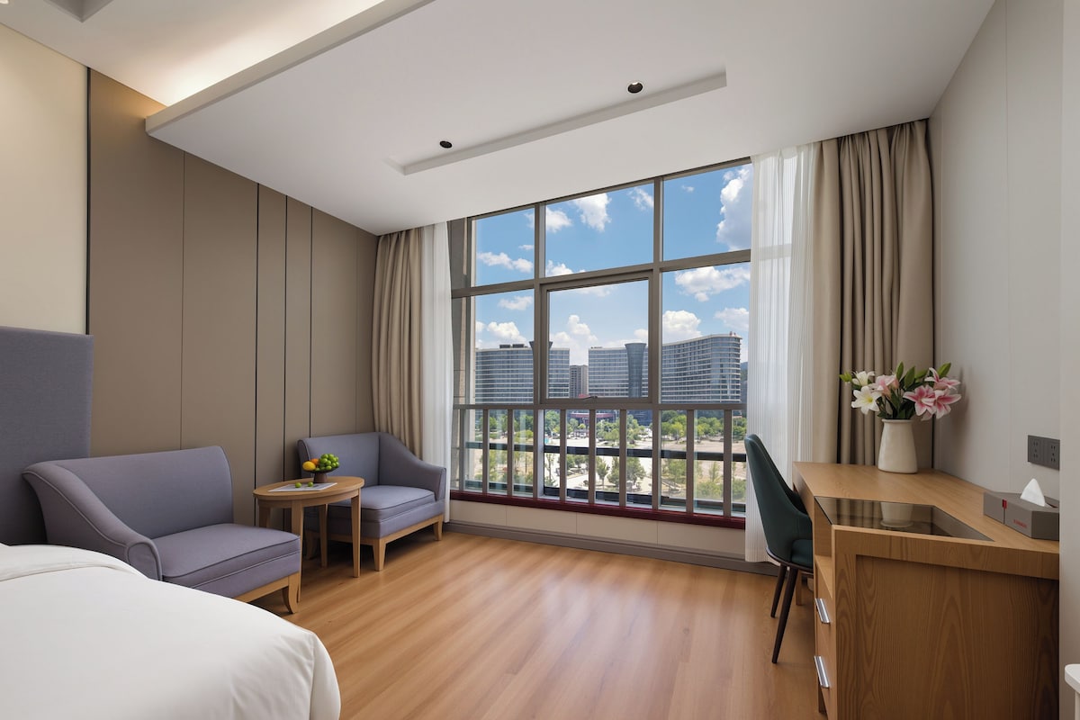 Una habitación de hotel con un ventanal grande, una cama, un escritorio y una zona de estar.