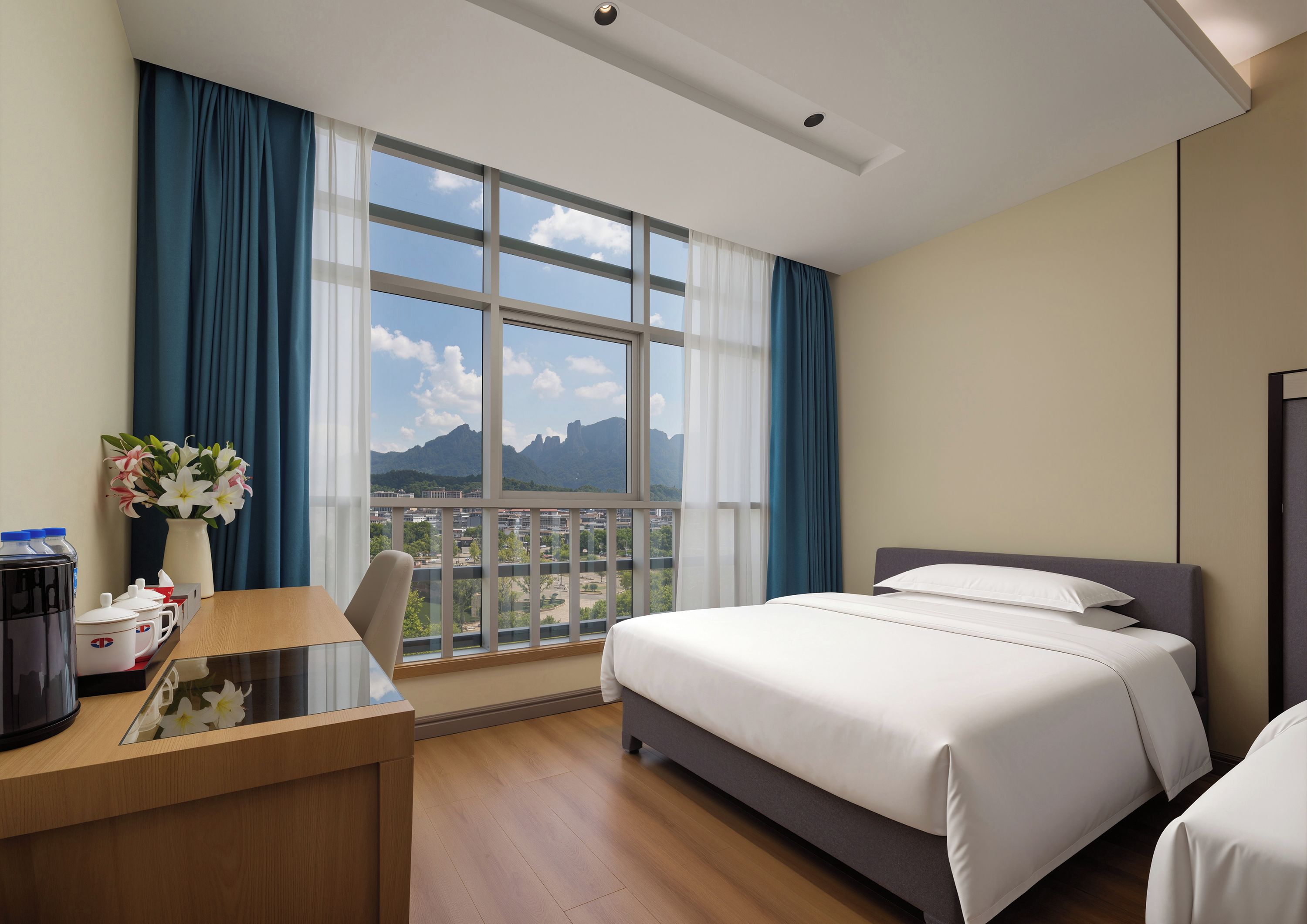 Habitación de hotel con una cama, un escritorio con cafetera, un florero con flores y vistas a las montañas a través de amplios ventanales.