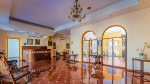 Un'accogliente hall d'albergo con pavimento in piastrelle lucide, arredi in legno, una reception e un lampadario.