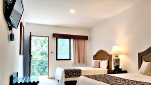 Camera d'albergo con due letti, una TV fissata al muro, una finestra con tende e una lampada sul comodino.