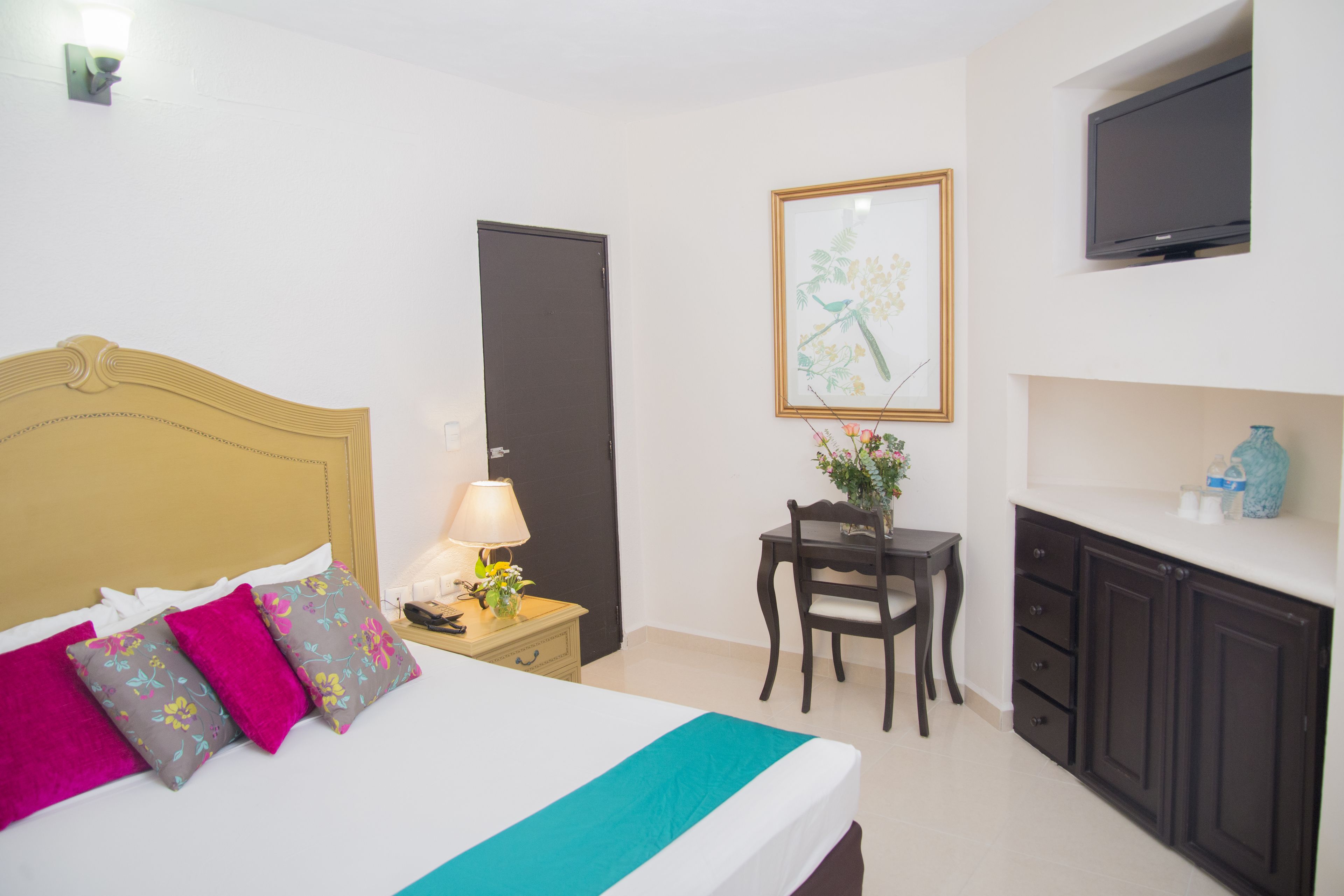 A hotel room with a bed, bedside table, lamp, chair, desk, TV, and cabinets.